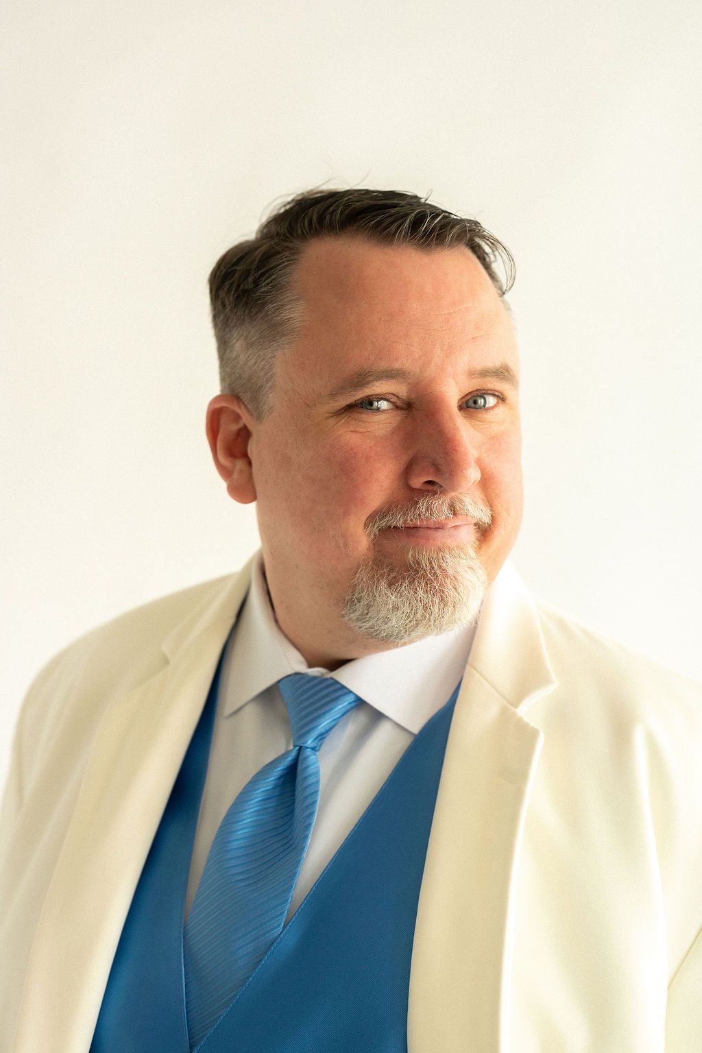 Joseph Mason in a cream jacket, blue waistcoat and blue tie, smiling.
