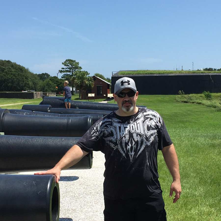 Sig. Alexander outdoors beside a row of old cannons, wearing a cap and sunglasses.