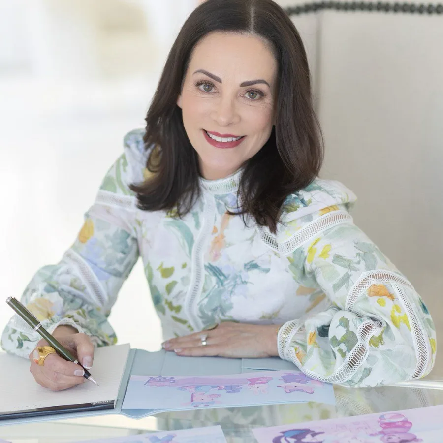 Brenda Gentile smiling at her writing desk, pen in hand, wearing a floral blouse.