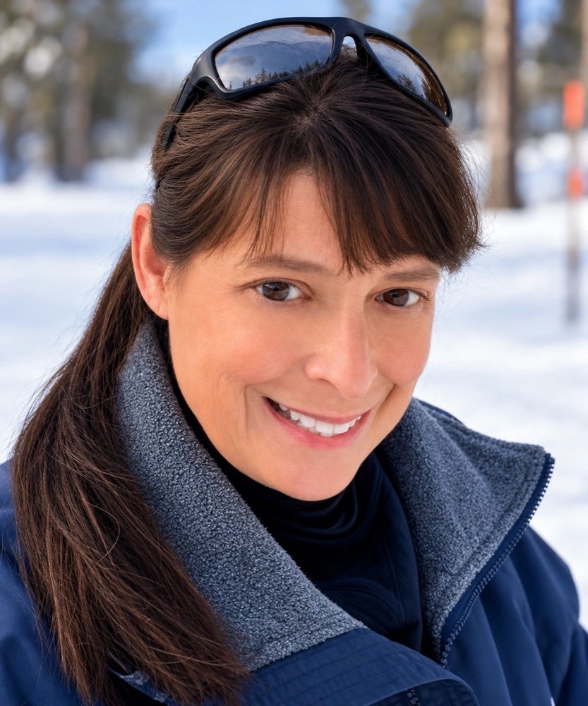 Portrait of D. R. Berlin smiling outdoors in the snow, sunglasses pushed up on her head.