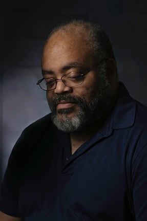 Portrait of G. Russell Gaynor, looking down, in low studio light.